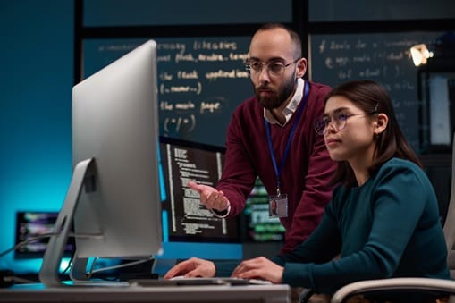 IT Development Supervisor Advising Trainee Portrait of bearded adult man as IT development supervisor advising young trainee in office and pointing at computer screen copy space